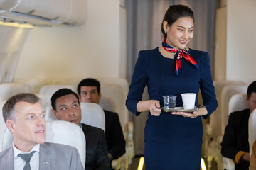 flight attendant serving water and cup of tea or coffee to passenger in airplane