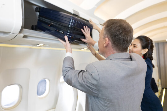 Flight Attendant Helping Passenger With Carry On Luggage To Overhead Bins