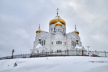 Orthodox white Cathedral church with spires, domes, a cross on a winter day and snow around in Russia