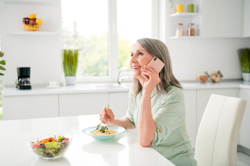 Obraz na płótnie Canvas Profile side view portrait of attractive cheerful grey-haired woman eating fresh homemade dinner talking on phone at home light white indoors