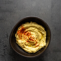 Top view of chickpea hummus  bowl decorated with olive oil and paprika on dark background