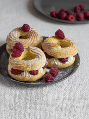 Cream puff rings eclairs choux decorated with fresh raspberries on grey plate, selective focus