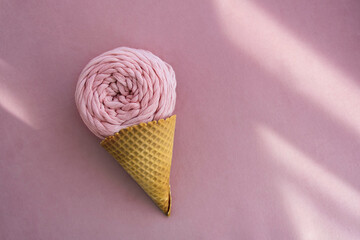 Top view of pink macrame yarn skein in ice cream waffle cone on a pink background with sunlight beams - obrazy, fototapety, plakaty