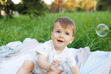 little cute baby sits on a blanket in the park on a green lawn