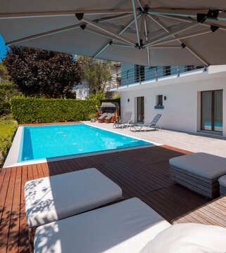 Large modern pool with two sun loungers for sunbathing and an open umbrella. View of the mountains of Switzerland