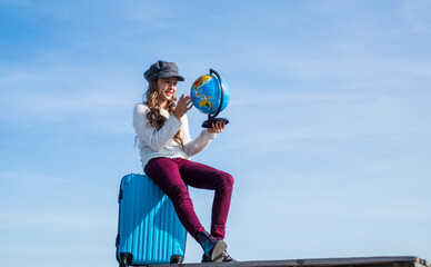 teen girl with globe and travel bag on sky background, copy space, traveling