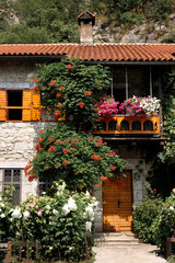 Fototapeta na wymiar stone house with tiled roof with flowering bushes nearby. background