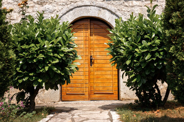 wooden doors of a stone house surrounded by laurel bushes.