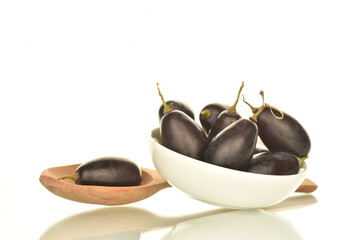Several berries of black grapes in a white saucer with a wooden spoon, close-up, isolated on white.