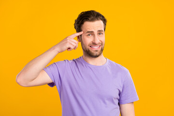 Photo of unhappy pretty young guy dressed purple t-shirt finger forehead isolated yellow color...