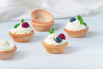 Mini tartlets with whipped cream and fresh berries, on a white table, blurred focus, horizontal, no people,