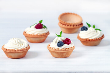Mini tartlets with whipped cream and fresh berries, on a white table, blurred focus, horizontal, no people,