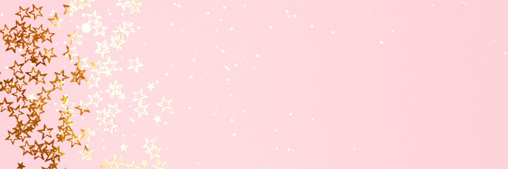 Banner with trendy gold colored stars confetti on a pink background with copyspace.