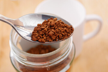 Closeup of spoon of instant coffee. Spoon of soluble coffee against the background of the white cup and coffee jar. Making breakfast concept