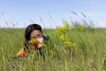 Brunette woman lies on the grass enjoying the smell of steppe flowers. Fresh natural summer, leisure and people concept.