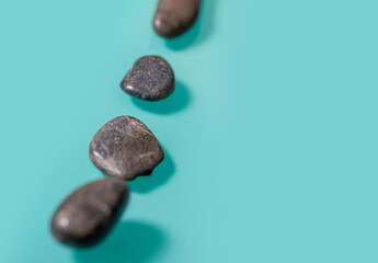 4 small black stones, similar to pebbles, lie diagonally on the left on a turquoise background.