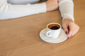 The woman on the wooden table holding Turkish coffee with your hands