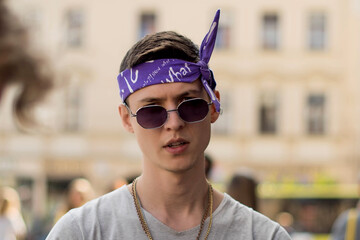 Positive male teenager with bandana dressed in street style clothes with chains around neck and...