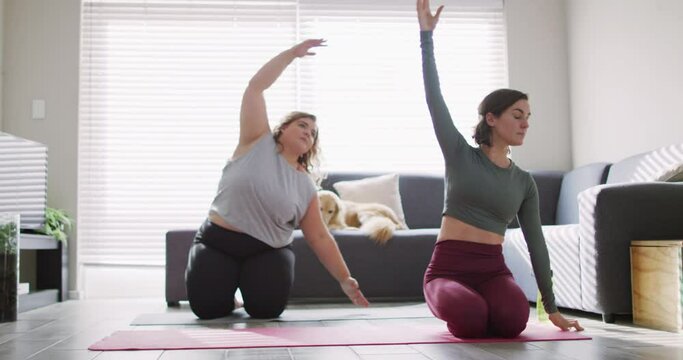 Caucasian lesbian couple keeping fit and stretching on yoga mat