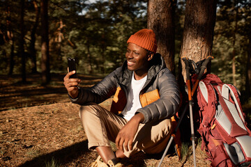 Smiling afro american guy talking to family on video call. Chilling on fresh air, trip to forest for camping and hiking. Time for adventures, exploring, travelling concept