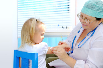 female doctor, pediatrician examines small child, 2-year-old girl with white hair, vaccinates,...