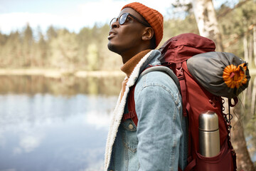 Guy astonished by magnificent nature. Afro american wanderer with backpack with tent ready for...