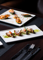Eggplant rolls with cheese, tomatoes and basil lie on a white plate in a restaurant