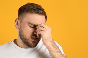 Obraz premium Man suffering from migraine on yellow background, space for text