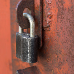 An old metal padlock painted black on a rusty steel door in red