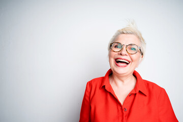 Cheerful elderly woman in glasses and in a red shirt laughs and smiles while looking at the camera