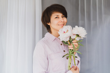 Sensual portrait of Mixed race smiling woman with pink peonies bouquet at white fabric background. Women's day, happy people.Selective focus, copy space.