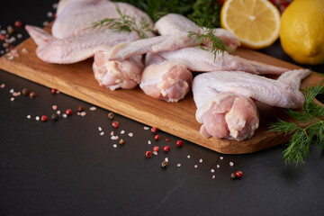 Raw chicken wings with ingredients for cooking. Raw meat. Chicken wings lie on a wooden board with vegetables and spices on a black background. background image, copy space text.