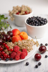 On a light background, a blurred image of a plate with raspberries, red and white currants, apricots, cherries and blueberries in a gravy boat.