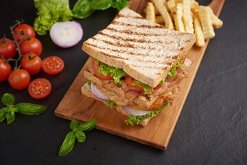 Club-sandwich with french fries. Sandwich with bacon, fried egg. Grilled and pressed toast with bacon, fried egg, tomato and lettuce served on wooden cutting board.