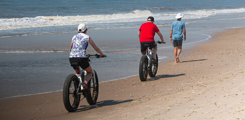 Couple riding fat wheel bikes passing a walker on the waters edge