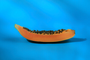 Fototapeta premium Foto de trozo de Papaya cortado con semillas sobre fondo celeste. Rebanada de Papaya cortada. Papaya Madura.