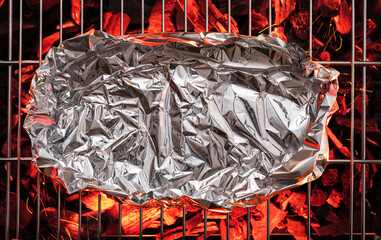 Some food in aluminum foil on  grate over hot pieces of coals. Top view.