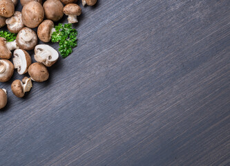 Brown colored edible mushrooms or cremini mushrooms on black table with herbs. Top view.