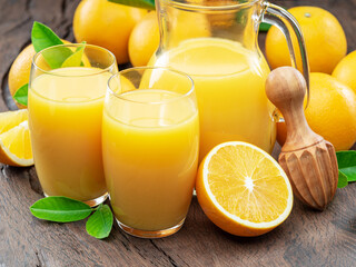 Glasses of fresh orange juice and orange fuits near them isolated on dark wooden background. Close up.