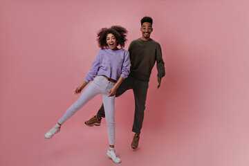 Happy couple in purple and brown outfits jumping on pink background. Brunette man and curly pretty woman dancing on isolated