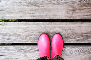 Pink puddle. Rain bright boots. Dirty safety shoes. Summer weather. Walking at mountains. Person feet. Rainy. Wood background