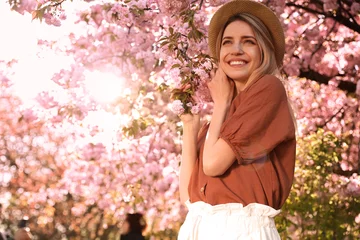 Fotobehang Young woman wearing stylish outfit near blossoming sakura in park. Fashionable spring look © New Africa