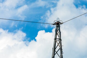 Warning light on a power pole. High voltage electric pylon against cloudy blue sky. Electricity...