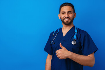 Handsome young male doctor in blue uniform with stethoscope against blue background