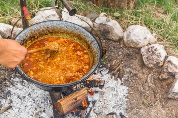 Metal cauldron boiling on a bonfire. Cooking on open fire, camping meal. Traditional preparation of...