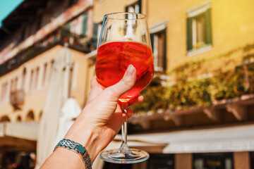 Female hand with glass of orange cocktail spritz on the background of old buildings. Alcoholic...