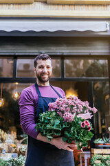Young businessman showing a pot of plants in front of his store. Vertical photography.