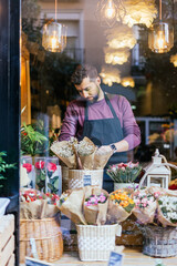 Flower shop owner placing bouquets of flowers in his shop showcase through a glass window.