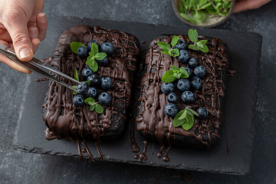 Pastry chef decorates brownie cake with blueberries and mint leaves