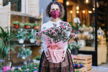 Young girl with mask showing a pot with plants in front of a flower store. Focus on the plants